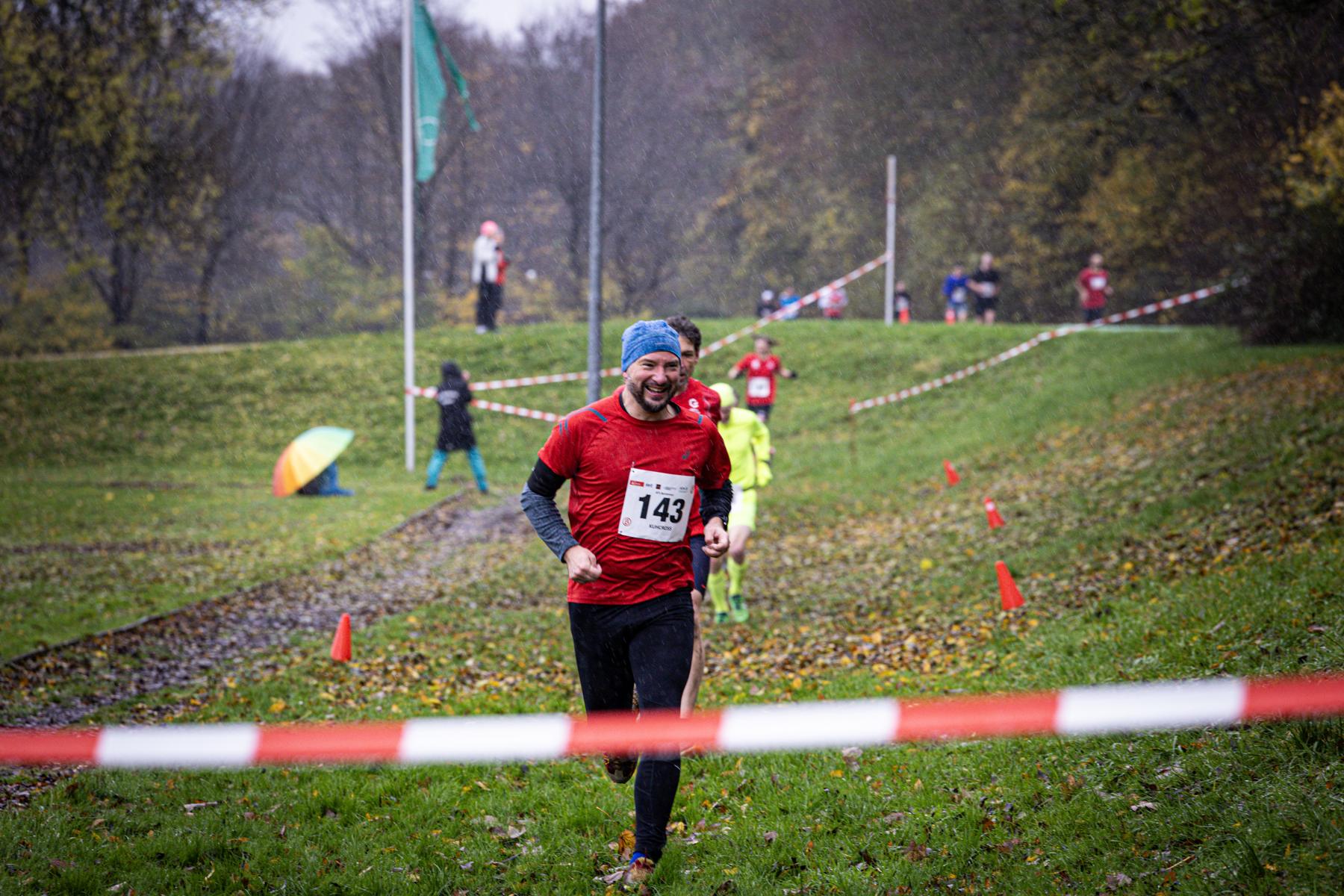 Lachender Läufer mit Startnummer 143 kommt im Regen den Deich herunter